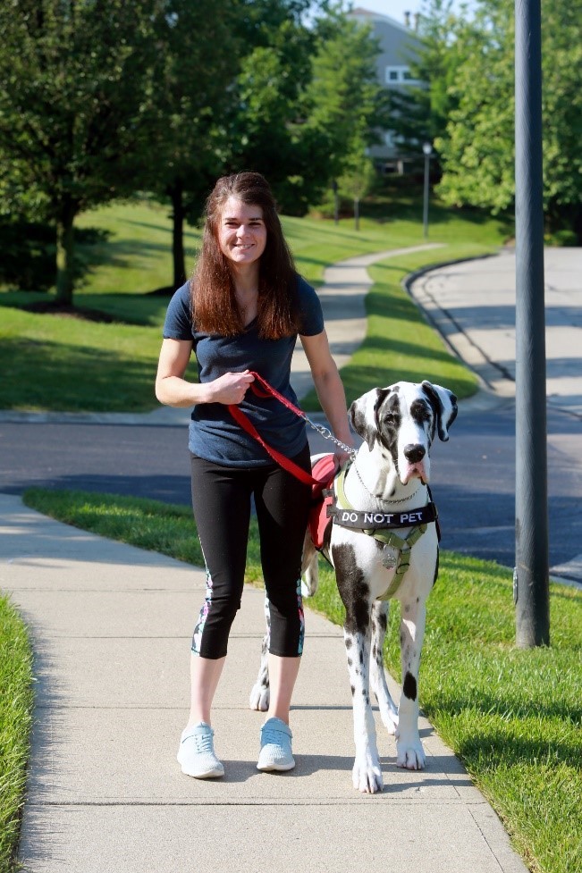 A young White woman walking with her large service dog.