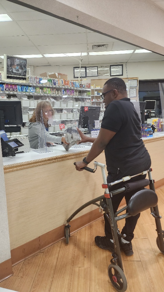 Young African American man with a walker picking up medications at the pharmacy counter.