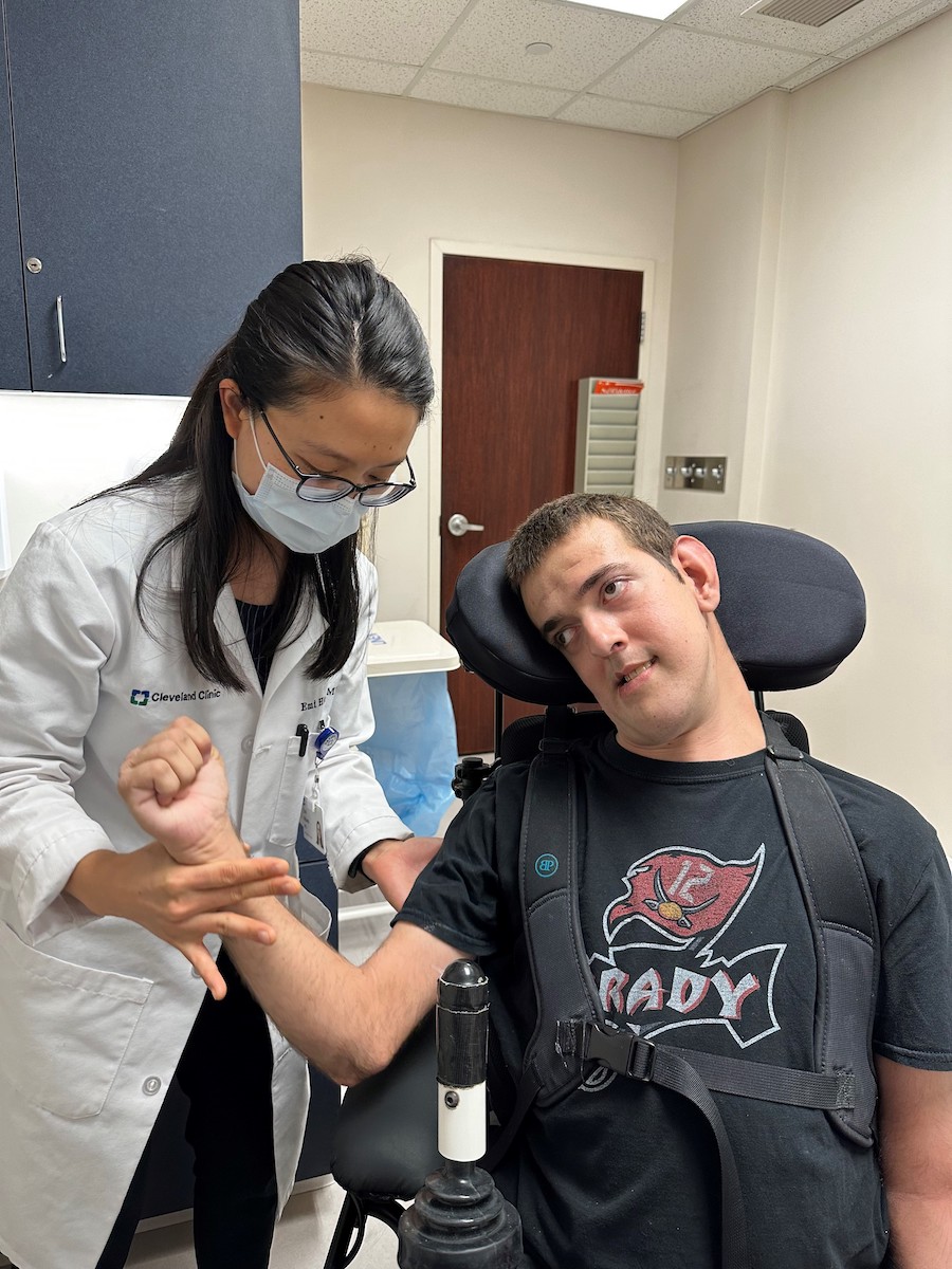 An Asian female physician examining a young white man in a wheelchair.