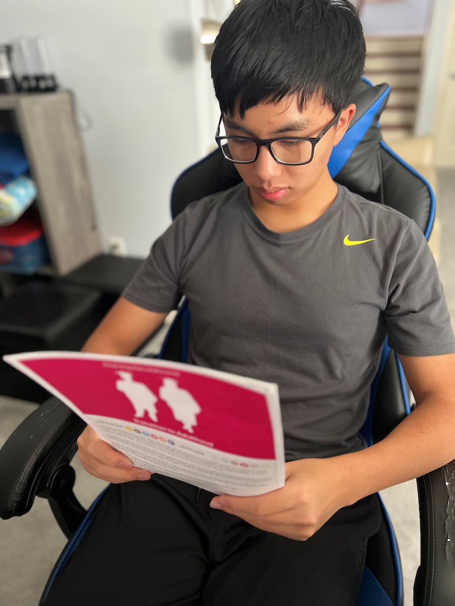 An Asian teenage male reading a paper on health care transition.