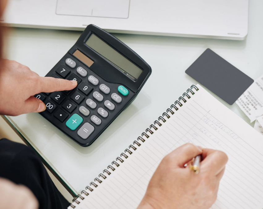 Someone writing in a notebook while using a calculator with their other hand