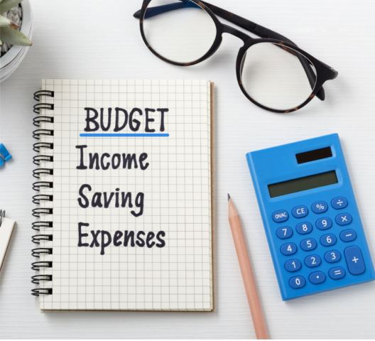 Glasses, a calculator, and a notebook with a pencil. The notebook reads Budget: income, savings, expenses in a list.