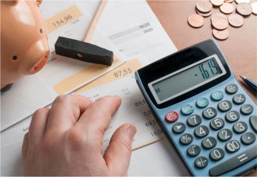 Someone's desk that shows a piggy bank in the corner and a person’s hand using a calculator to do the math on their expenses