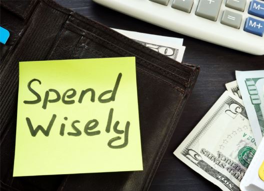 Someone’s wallet with money in it and a post-it note on it that reads spend wisely