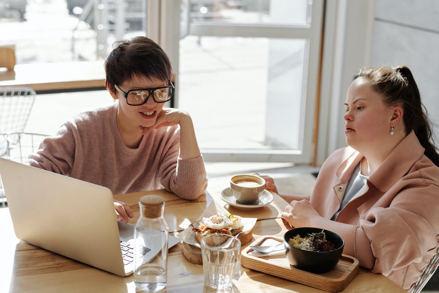 Two people talking over a meal while looking at a computer screen.