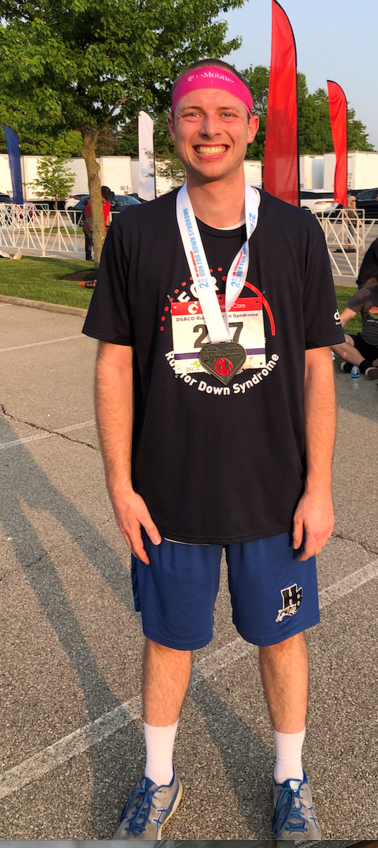 White man standing with a racing medal smiling proudly.