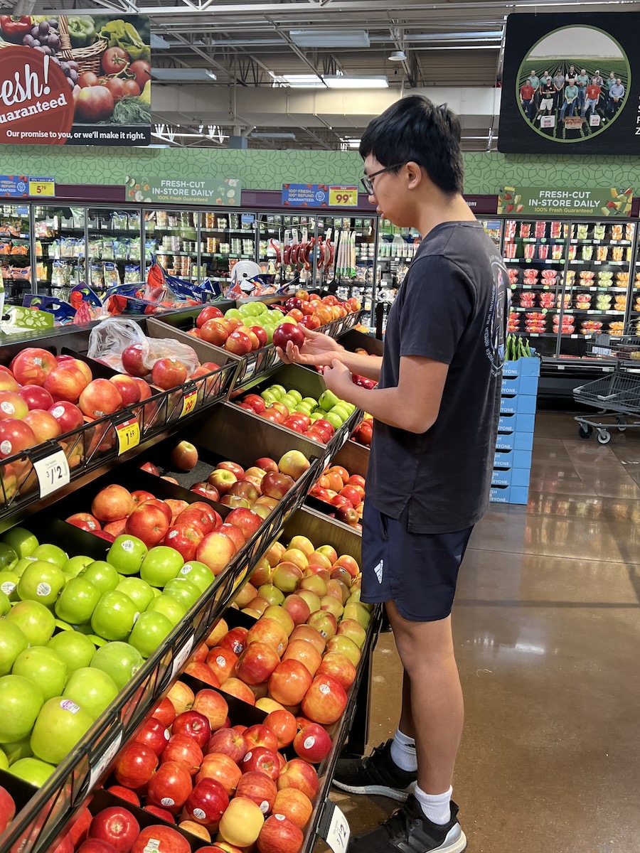 Young Asian male looking at different kinds of apples in the grocery store