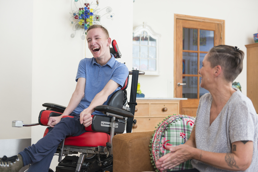 A young White man in a wheelchair smiling beside a White female.