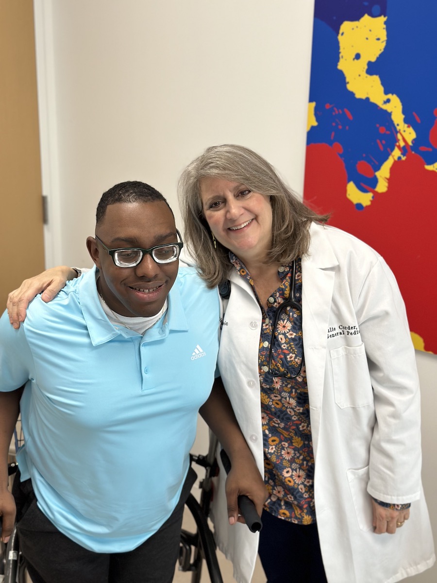 A young African American man standing and smiling with a White female doctor.