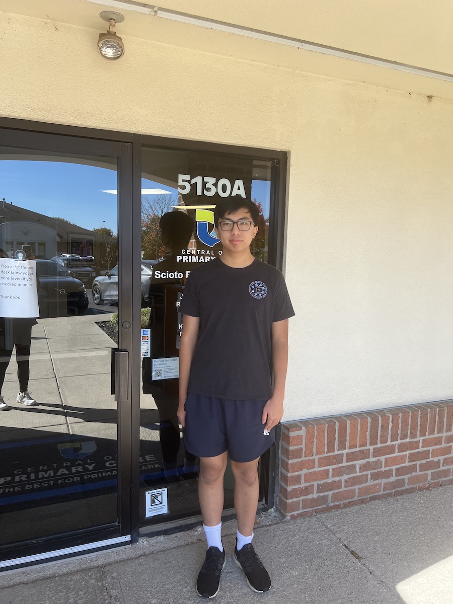 A young Asian man standing in front of a medical office building.