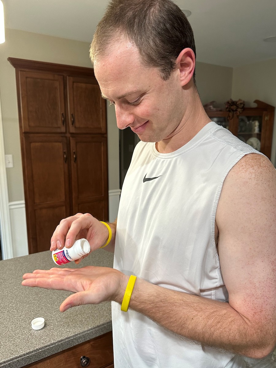 A young white man taking medication out of a medicine bottle.