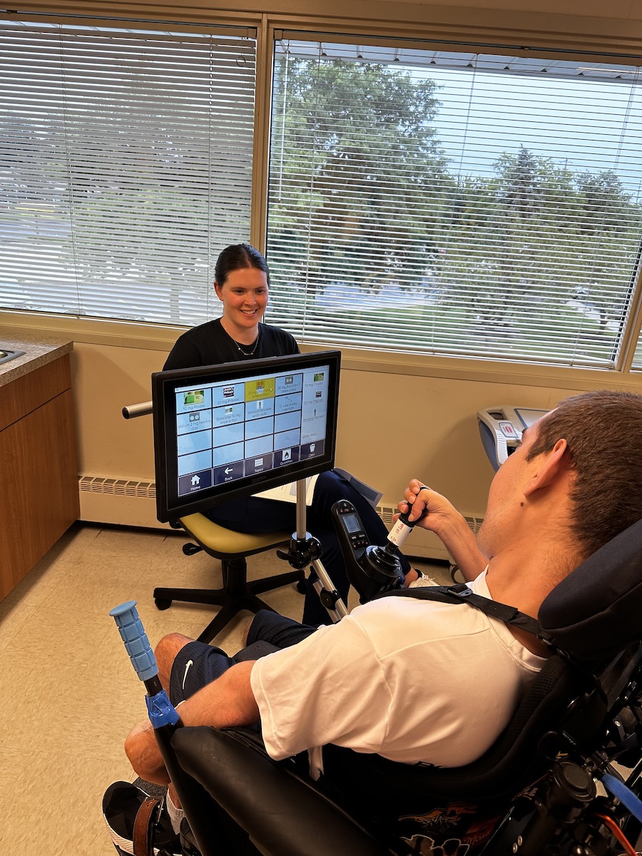 A young White man using a communication device to talk with a White female nurse.