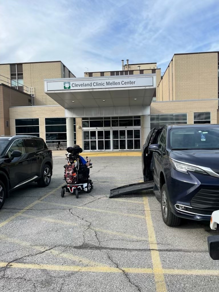 A person exiting a van in an accessible parking space using wheelchair to enter a medical building.