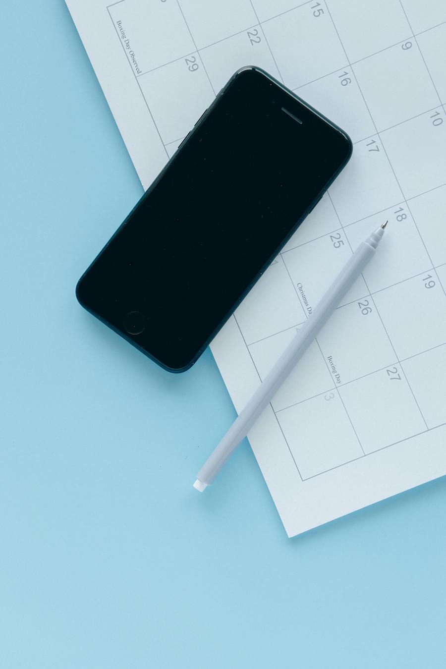 A phone, pen, and calendar on a table.