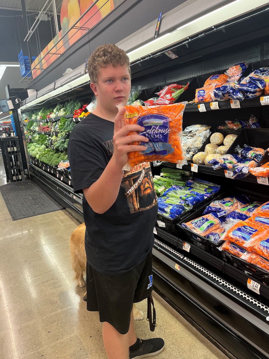 Young white male holding a bag of carrots at a grocery store..