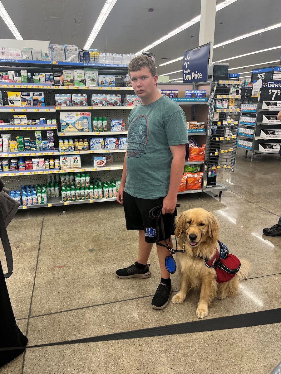 A young white male with his service dog standing in line at the pharmacy.