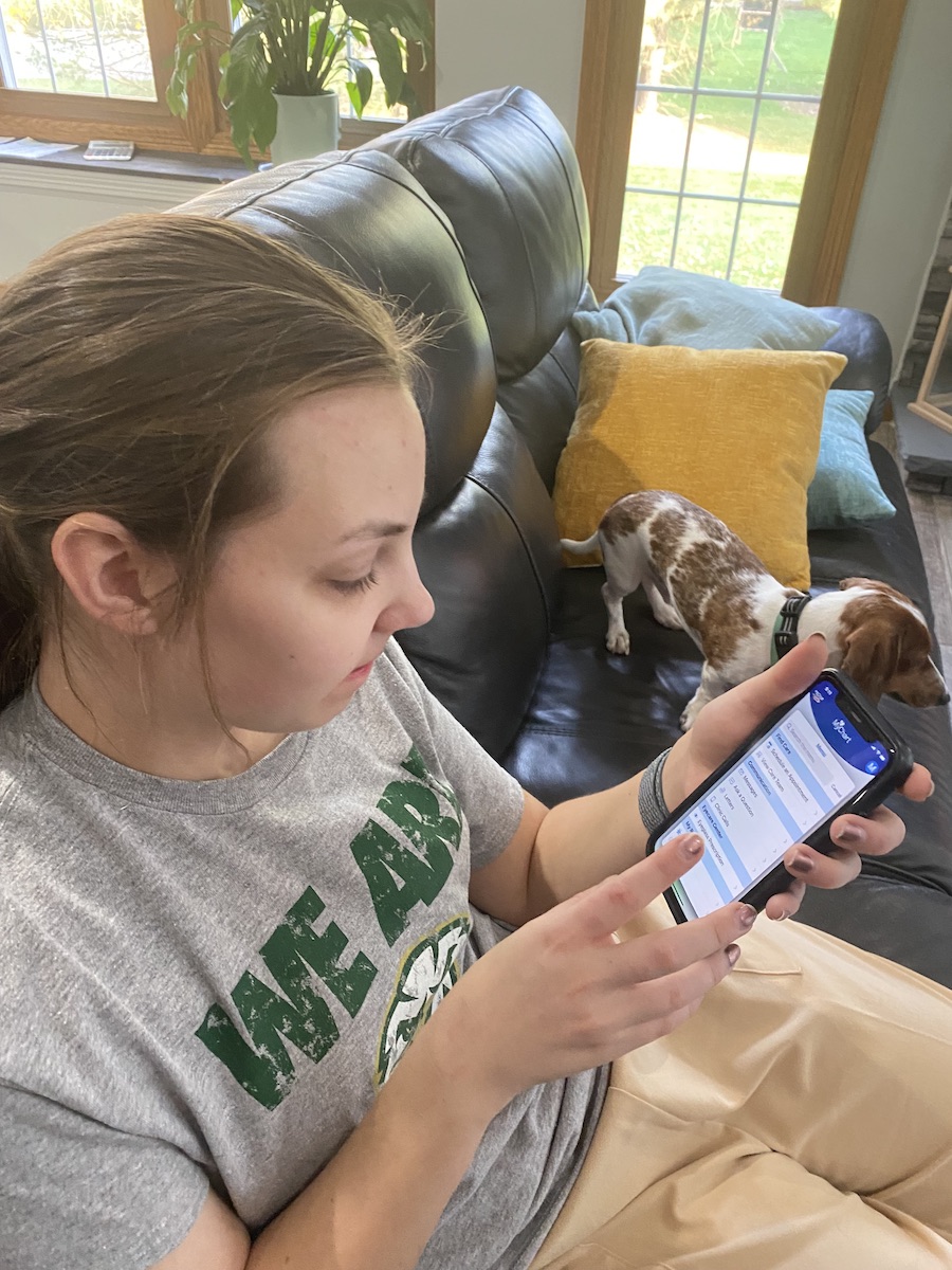 Young white woman sitting on a couch, using an app on her phone to organize medications.