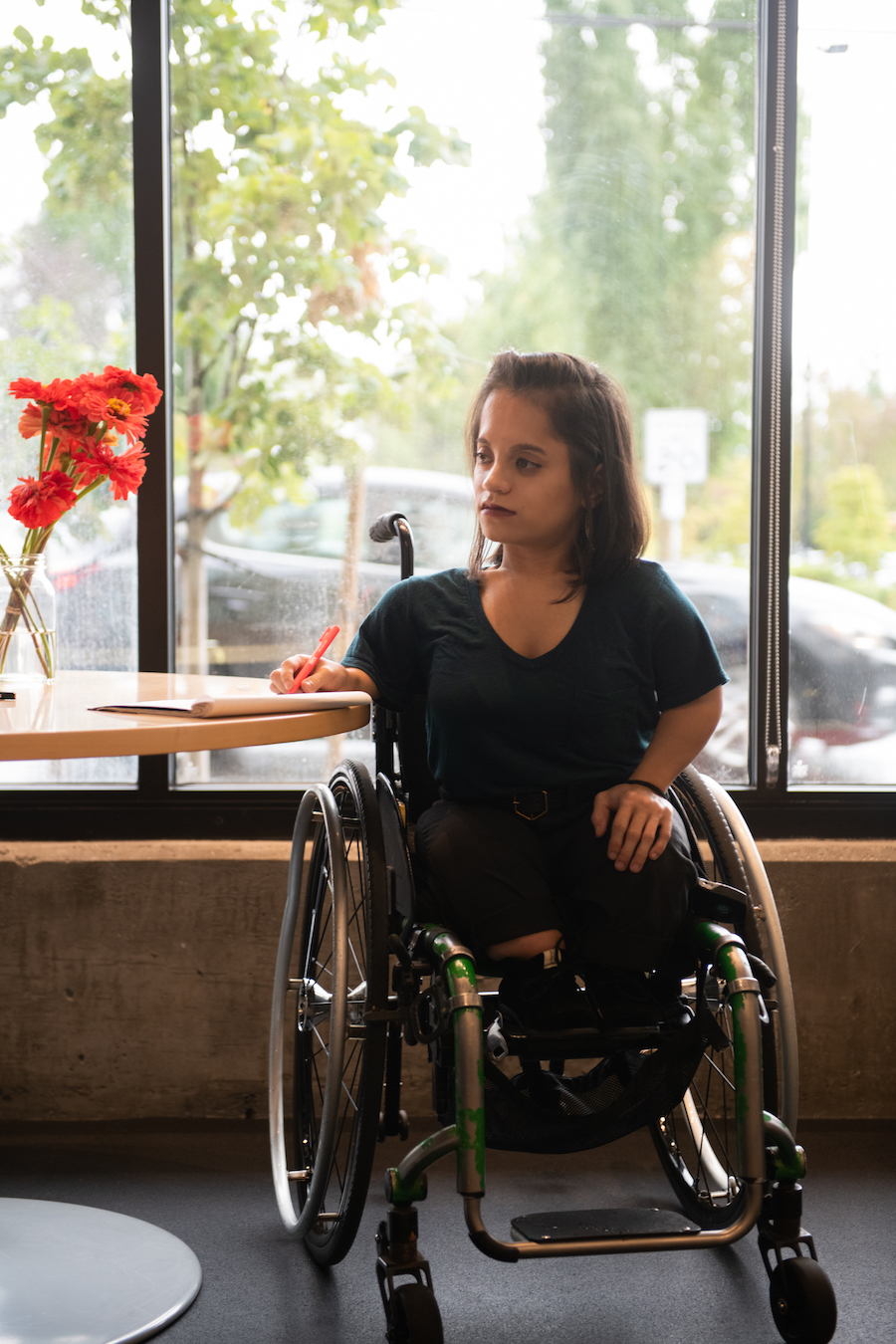 A young White woman in a wheelchair sitting at a table and writing on a piece of paper.