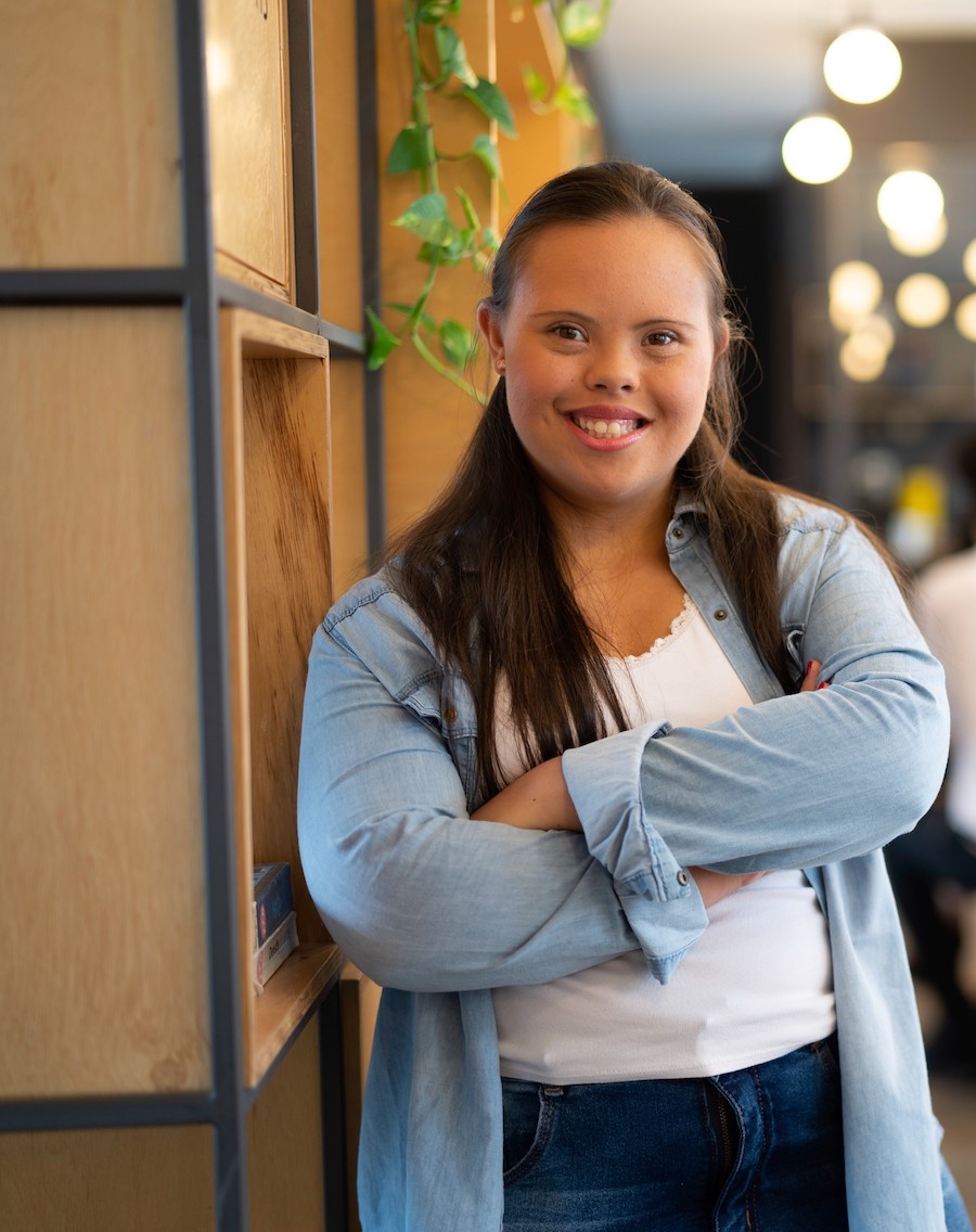 Young woman leaning against a wall and smiling confidently.