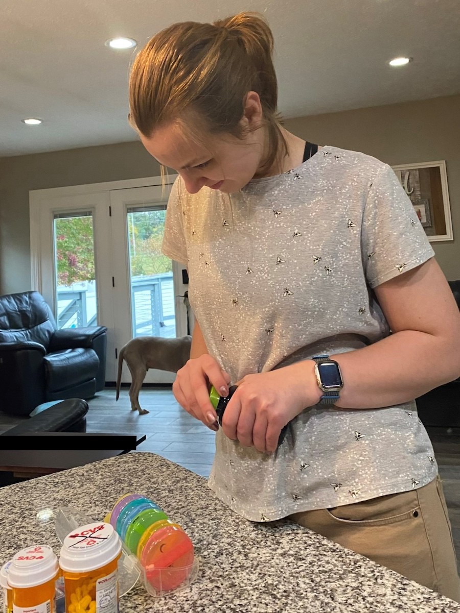 A young white woman looking at different medication bottles on the counter in her home.