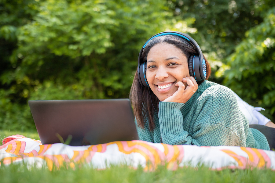 A young African American woman lying in the grass smiling with her headphones on.