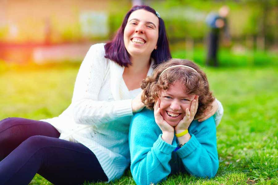 Two White women sitting on grass smiling and having fun.